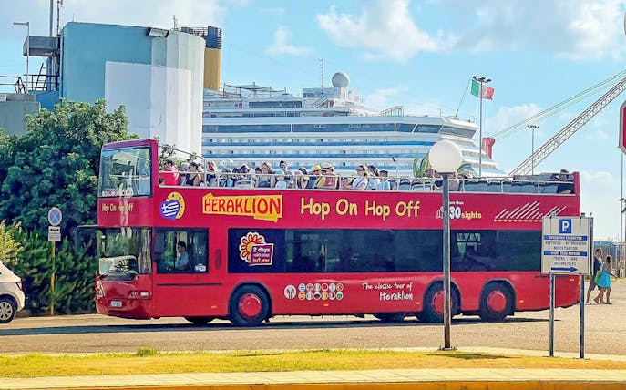 Heraklion Hop-On Hop-Off bus with tourists near a cruise ship.