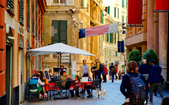 Walking dinner tour in Genoa with people dining at an outdoor café on a narrow street.