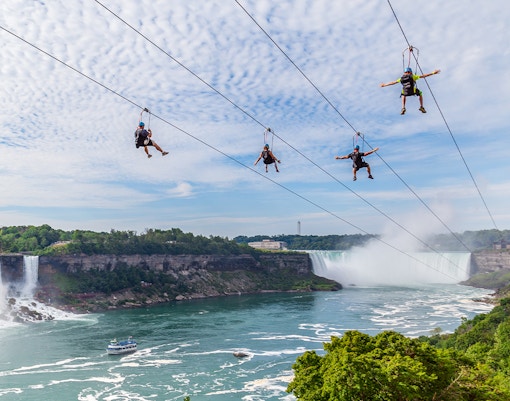 People zip lining over Niagara Falls with mist and waterfall in the background.
