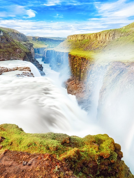 Gullfoss waterfall cascading over rocky cliffs in Iceland with a rainbow.