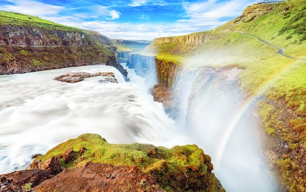 Gullfoss waterfall cascading over rocky cliffs in Iceland with a rainbow.