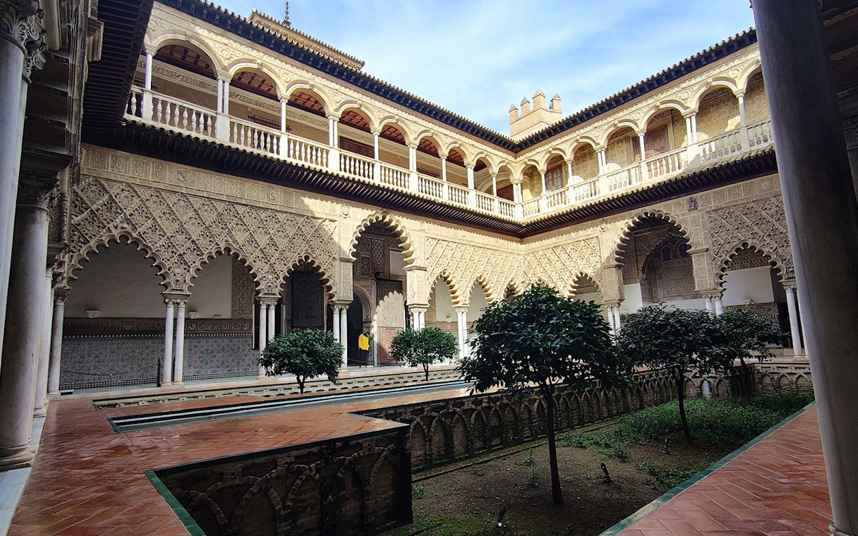 Alcázar courtyard with intricate arches and lush greenery, Seville guided tour.