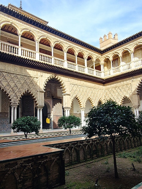 Alcázar courtyard with intricate arches and lush greenery, Seville guided tour.