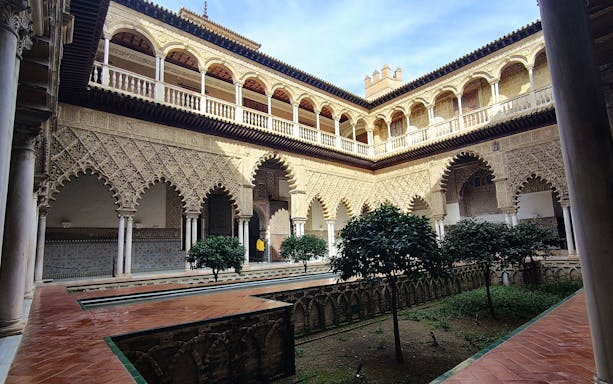 Alcázar courtyard with intricate arches and lush greenery, Seville guided tour.