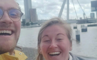 Smiling tourists with Erasmus Bridge in Rotterdam background.