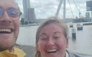 Smiling tourists with Erasmus Bridge in Rotterdam background.