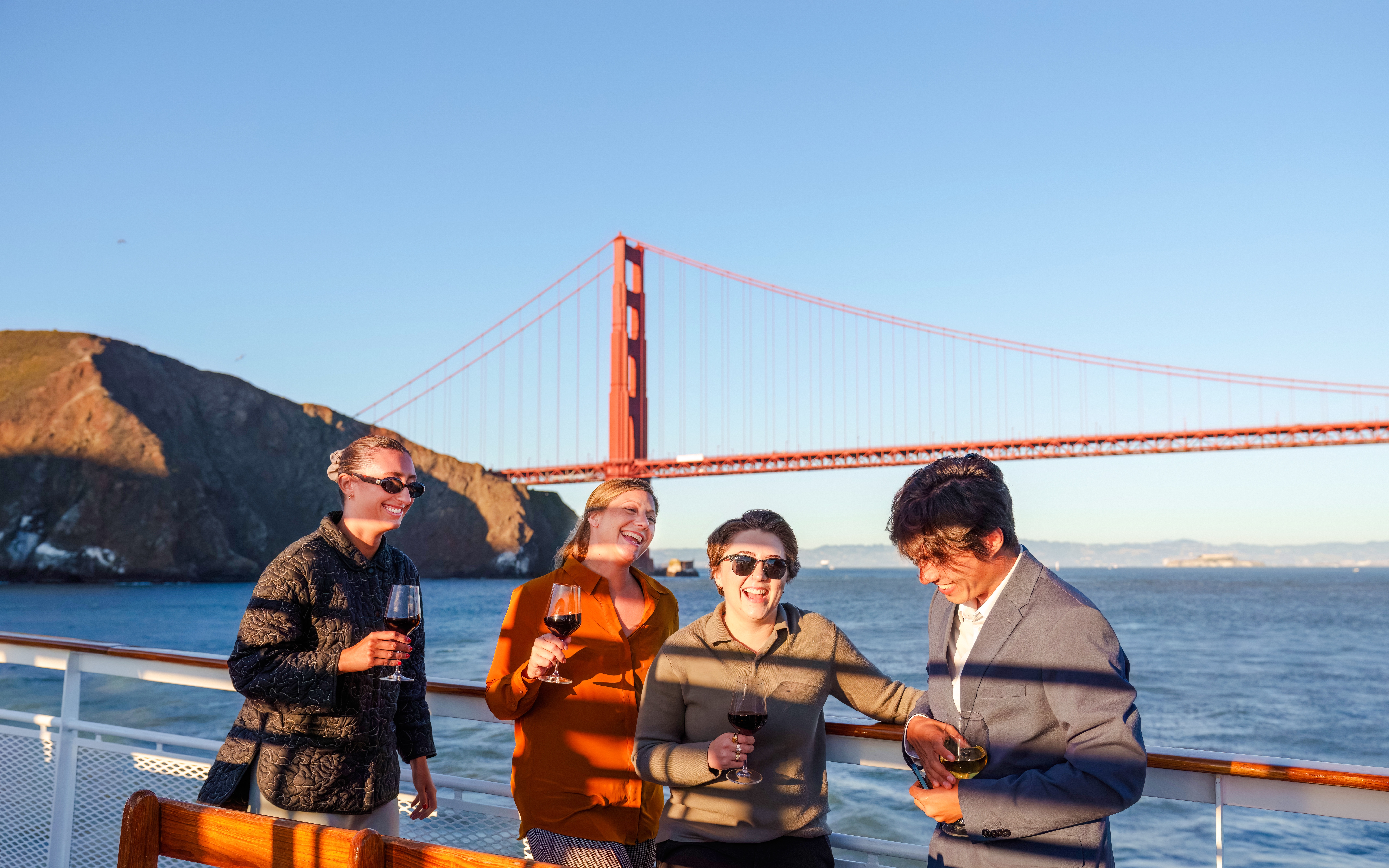 Group enjoying wine on a San Francisco dinner cruise with Golden Gate Bridge in the background.