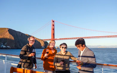 Group enjoying wine on a San Francisco dinner cruise with Golden Gate Bridge in the background.