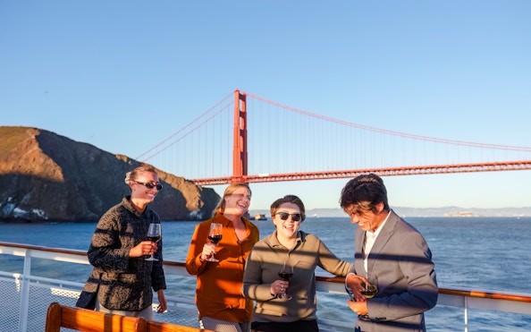 Group enjoying wine on a San Francisco dinner cruise with Golden Gate Bridge in the background.