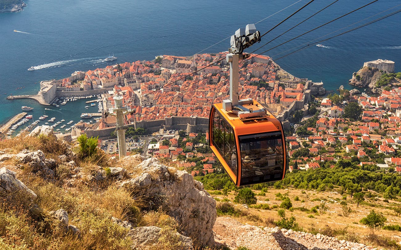 Cable car ascending over Dubrovnik with view of Old Town and Adriatic Sea.