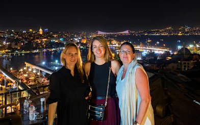 Guests enjoying rooftop views of Istanbul at night with city lights and Bosphorus Bridge.
