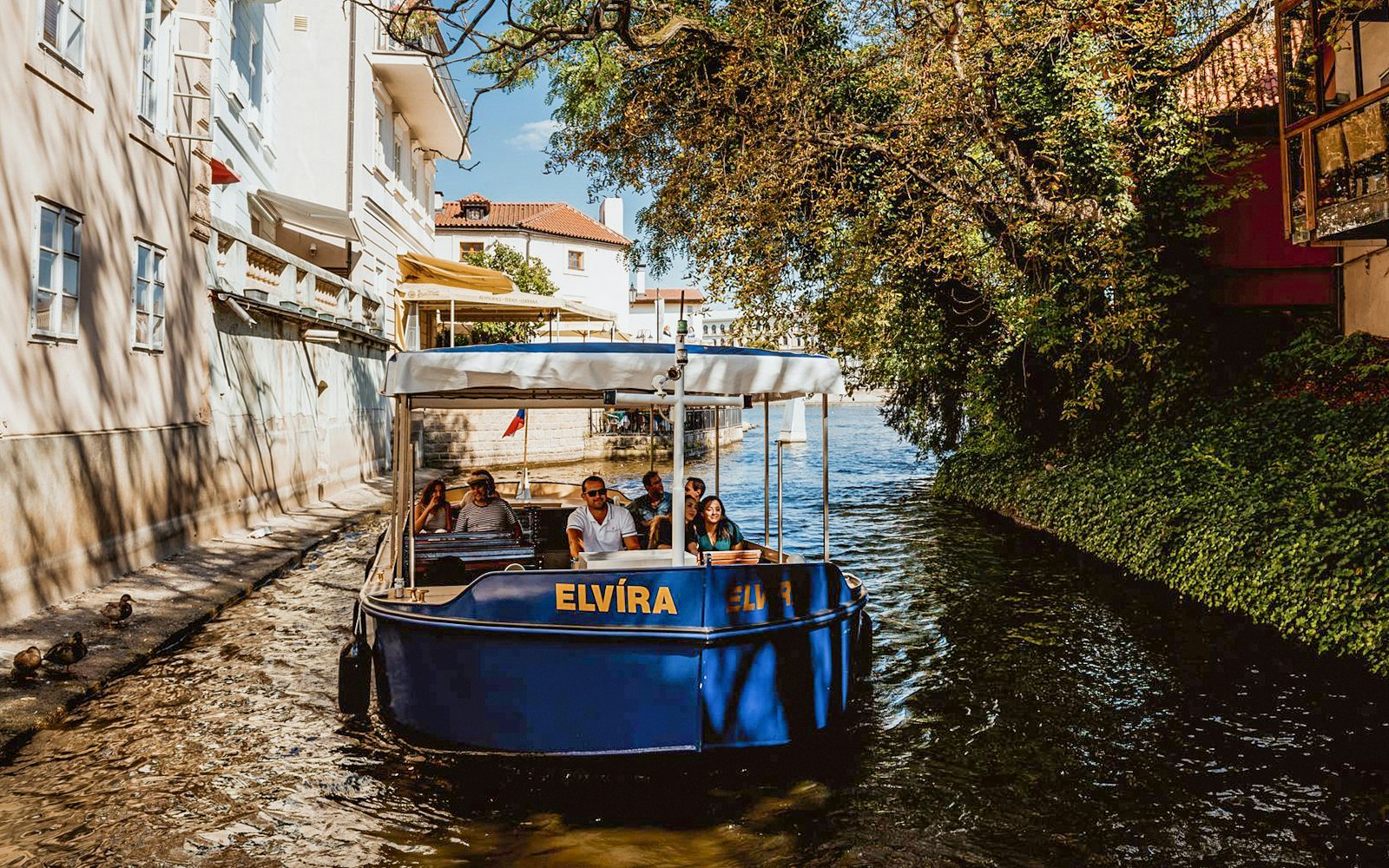 Sightseeing cruise boat navigating Devils Channel in Prague with historic buildings in the background.