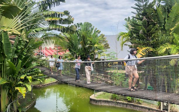 Visitors walking on a bridge at Koisaan Cultural Village, surrounded by lush greenery.