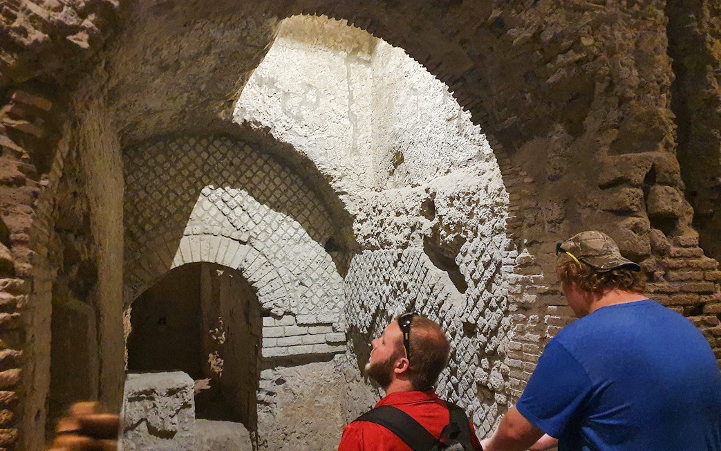Tourists exploring ancient underground ruins in Naples, Italy during a guided city tour.