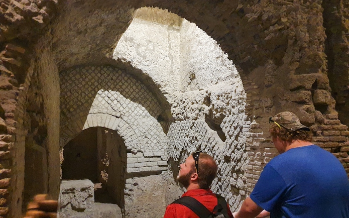 Tourists exploring ancient underground ruins in Naples, Italy during a guided city tour.