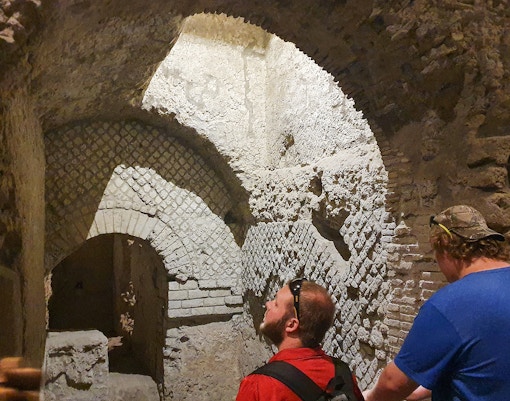Tourists exploring ancient underground ruins in Naples, Italy during a guided city tour.
