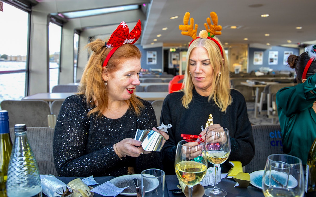 Guests enjoying Christmas lunch on Thames River cruise with festive headbands.