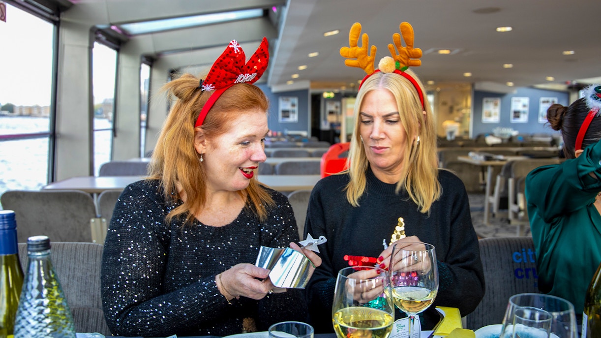 Guests enjoying Christmas lunch on Thames River cruise with festive headbands.