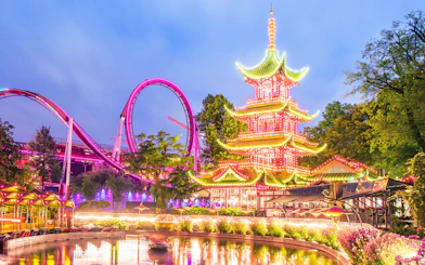 Tivoli Gardens illuminated pagoda and roller coaster at dusk.
