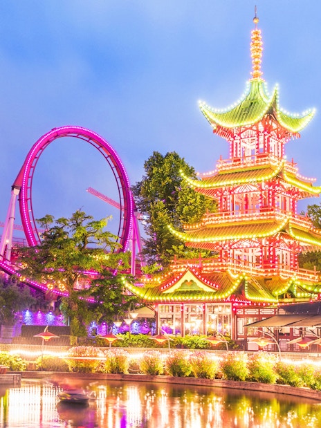 Tivoli Gardens illuminated pagoda and roller coaster at dusk.