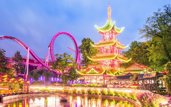 Tivoli Gardens illuminated pagoda and roller coaster at dusk.