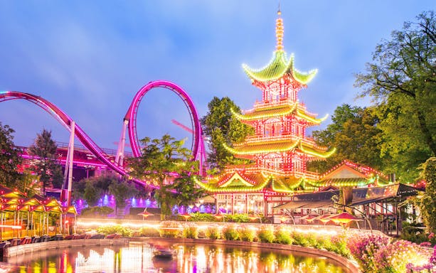 Tivoli Gardens illuminated pagoda and roller coaster at dusk.
