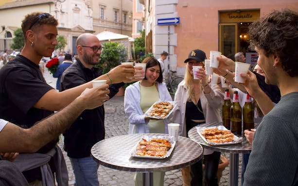 Group enjoying pizza and drinks during a food tour in Trastevere, Rome.