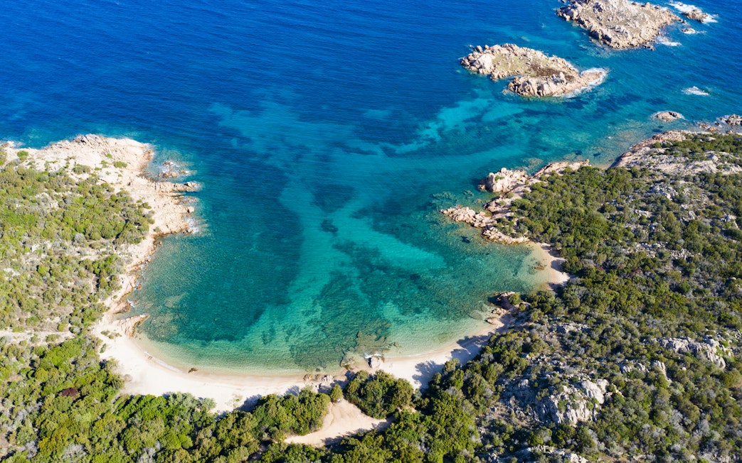 Aerial view of a secluded beach and turquoise waters on the Emerald Coast, Italy.