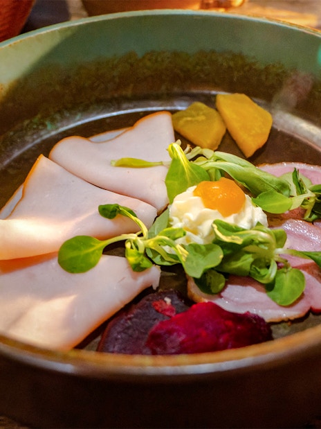 Medieval dinner show appetizer plate with meats, greens, and pickled vegetables.