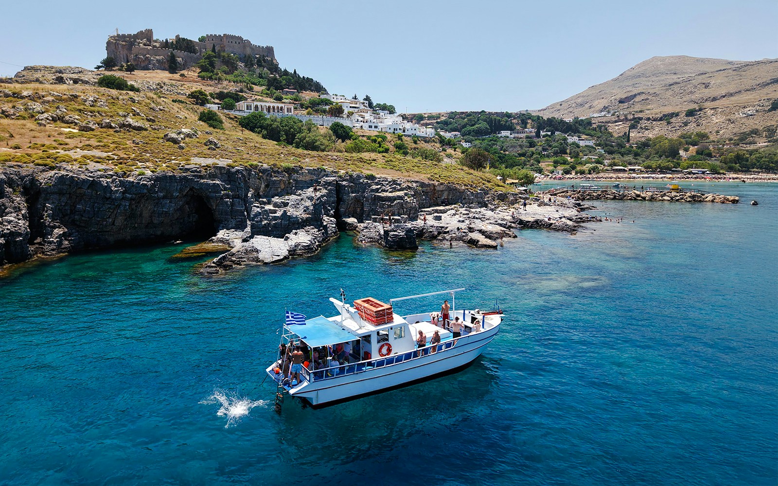 Boat cruising near Lindos cliffs with turquoise sea water.