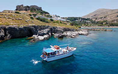 Boat cruising near Lindos cliffs with turquoise sea water.