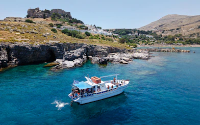 Boat cruising near Lindos cliffs with turquoise sea water.