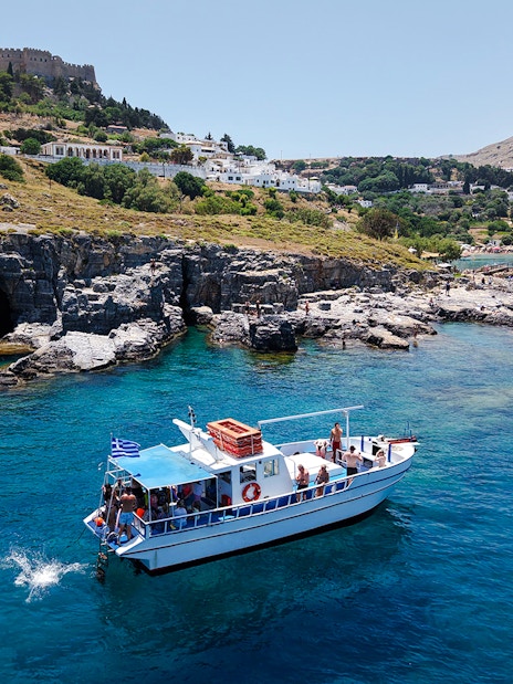 Boat cruising near Lindos cliffs with turquoise sea water.