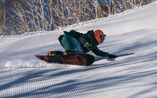 Snowboarder carving down a groomed slope in Niseko, Japan.