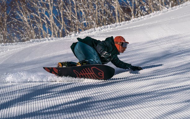 Snowboarder carving down a groomed slope in Niseko, Japan.