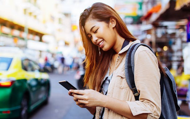 Traveler using smartphone on a busy street in Thailand.