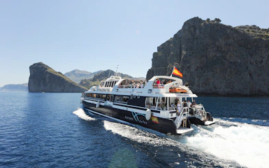 Boat cruising along Mallorca's rocky coastline during sightseeing tour.