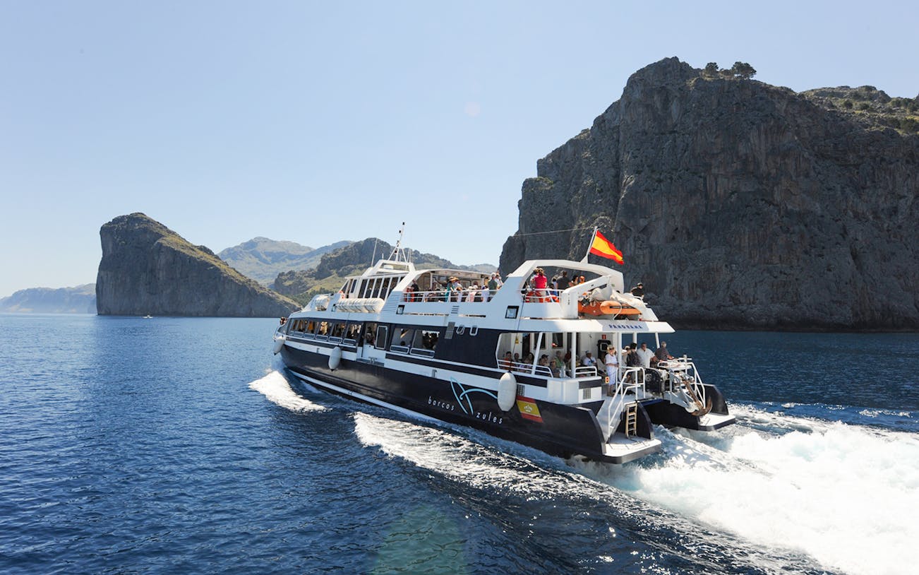 Boat cruising along Mallorca's rocky coastline during sightseeing tour.
