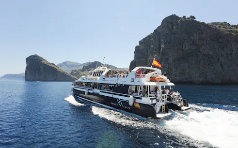 Boat cruising along Mallorca's rocky coastline during sightseeing tour.