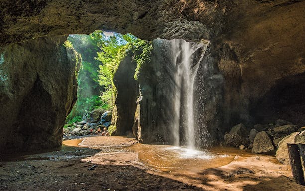 Gushing waterfall inside Goa Raja cave, Ubud, surrounded by lush greenery.