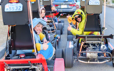 Friends in costumes sitting in go-karts, Osaka street tour.
