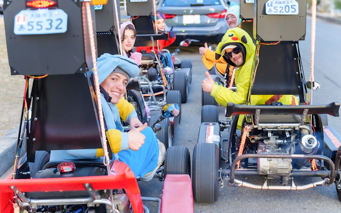 Friends in costumes sitting in go-karts, Osaka street tour.