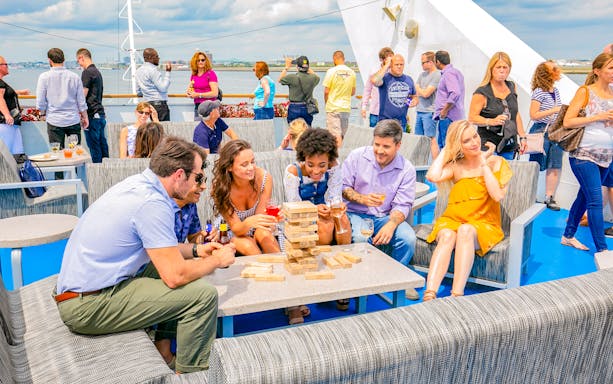 People enjoying drinks and games on a New York party cruise deck.