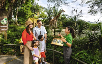 Family with guide at Singapore Zoo, Mandai Wildlife Reserve, with giraffe in background.