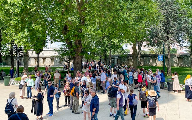 Tourists gather in a lush garden near historic Istanbul palace walls.