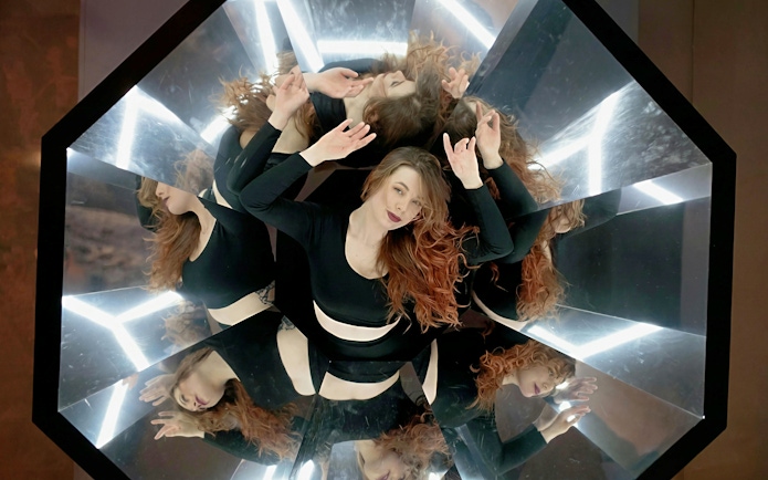 Person surrounded by mirrors creating multiple reflections at the World of Illusions exhibit.