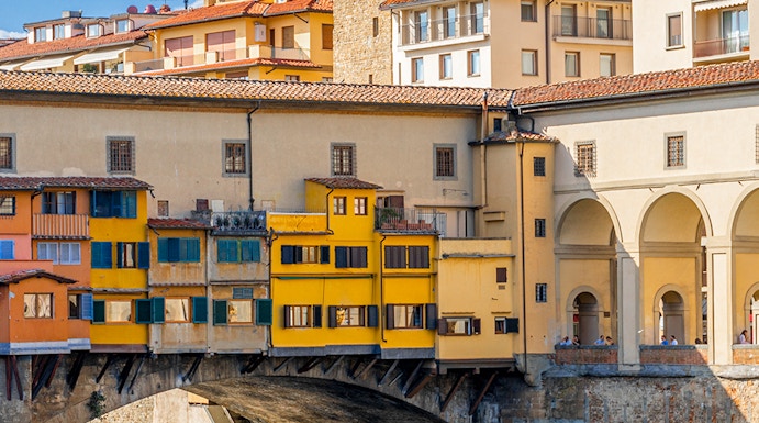 Vasari Corridor above Ponte Vecchio in Florence, Italy, with colorful buildings and river below.