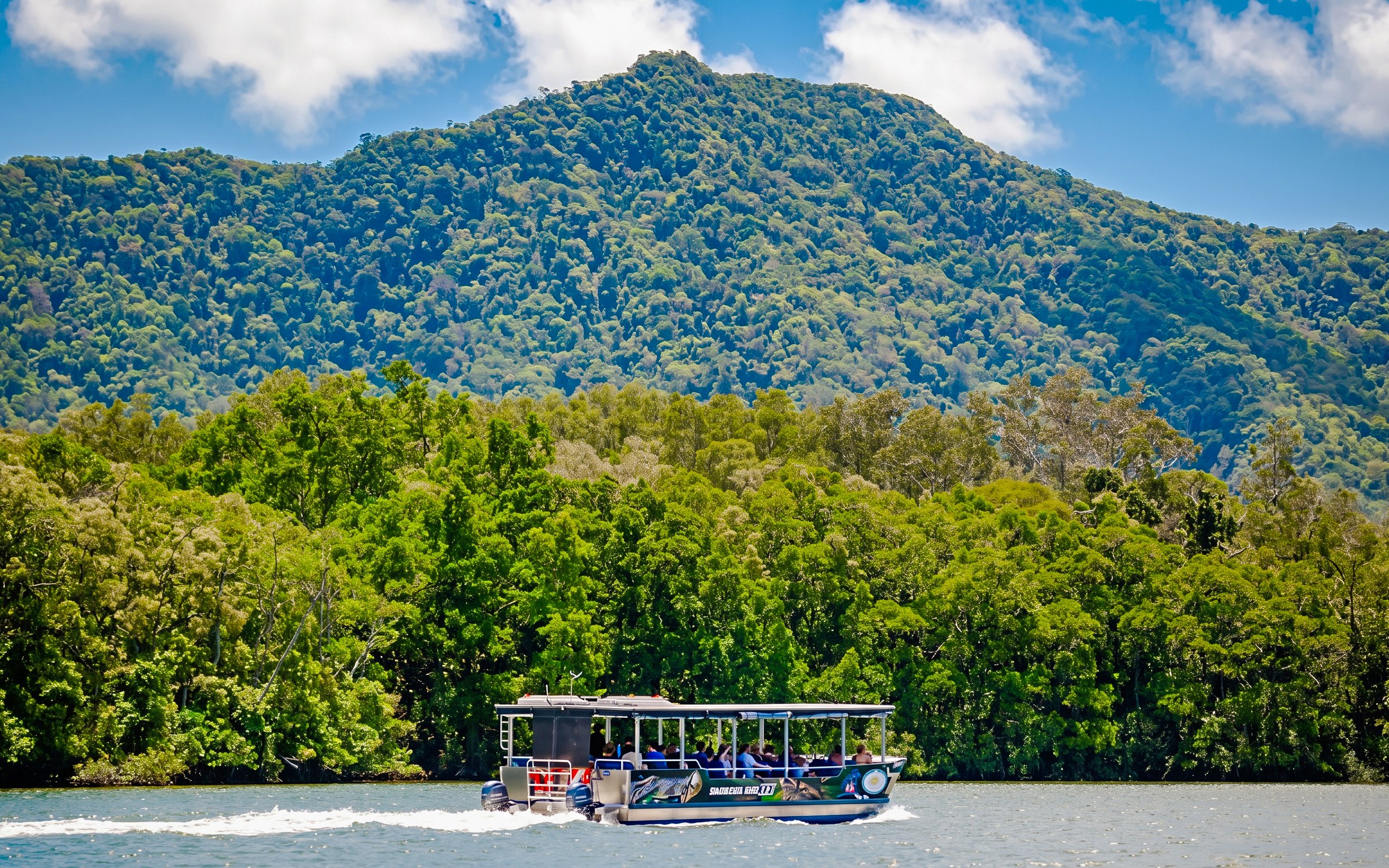 Boat cruising on Daintree River with lush forest and mountain backdrop, Bruce Belchers Daintree River Cruises.