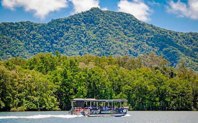 Boat cruising on Daintree River with lush forest and mountain backdrop, Bruce Belchers Daintree River Cruises.
