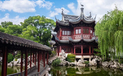 Traditional pavilion and bridge in Yu Garden, Shanghai, China, surrounded by lush greenery.